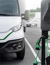 Un camión híbrido blanco estacionado junto a un punto de recarga